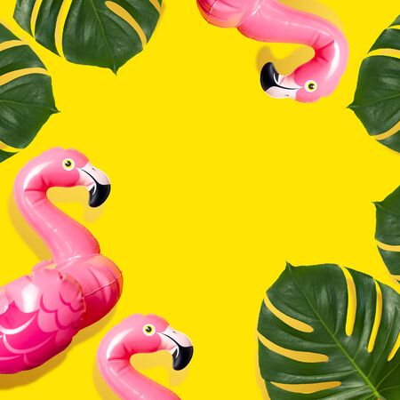 Creative summer beach concept. Inflatable pink mini flamingo and tropical leaf monstera on yellow background, pool float party. Flat lay copy space. Flamingo Trend Inflatable Toy. Summer background.の写真素材