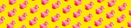 Creative summer beach concept. Pattern from Inflatable pink mini flamingo on yellow background, pool float party. Flat lay, copy space. Flamingo Trend Inflatable Toy. Summer background.の写真素材