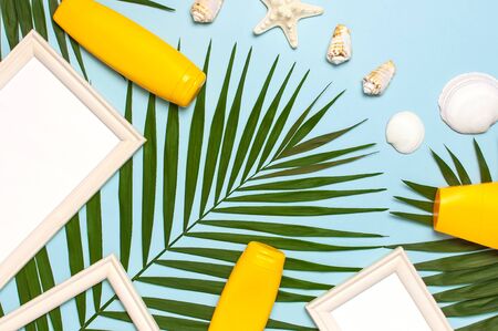 Summer fashion flat lay. Tropical palm leaves sunscreen white photo frame seashells starfish on blue background. Top view copy space. Sun protection. Summer background, vacation, travel concept.の写真素材