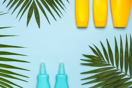 Yellow and blue bottles of sunscreen cream, tropical palm leaves on bright blue background top view flat lay copy space. Sun protection. Summer background, vacation, travel concept.の写真素材