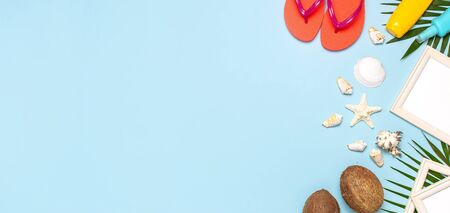 Summer fashion flat lay. Coral flip flops tropical palm leaves sunscreen white photo frame coconut seashells starfish on blue background. Top view copy space. Creative vacation background.の写真素材