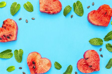 Creative summer food concept. Frame of Juicy slices of ripe red watermelon in the shape of a heart and mint leaves on blue background. Flat lay, top view, copy space. Watermelon pattern.の写真素材