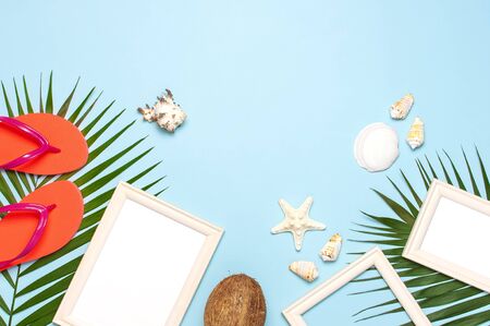 Summer fashion flat lay. Coral flip flops tropical palm leaves sunscreen white photo frame coconut seashells starfish on blue background. Top view copy space. Creative vacation background.の写真素材