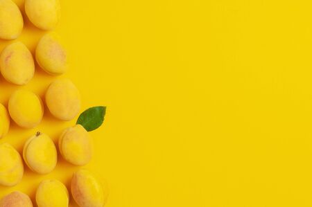 Ripe fresh apricots fruits with green leaves on yellow background. Flat lay, top view, copy space.の写真素材