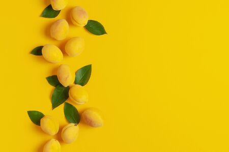 Ripe fresh apricots fruits with green leaves on yellow background. Flat lay, top view, copy space.の写真素材
