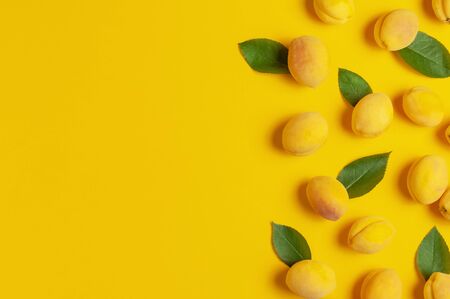 Ripe fresh apricots fruits with green leaves on yellow background. Flat lay, top view, copy space.の写真素材