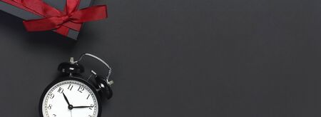 Black retro alarm clock and gift box with red ribbon on gray dark backgroundの写真素材
