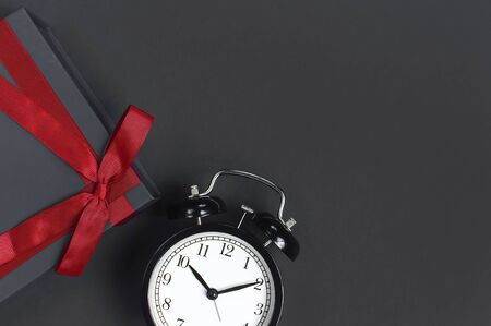 Black retro alarm clock and gift box with red ribbon on gray dark backgroundの写真素材