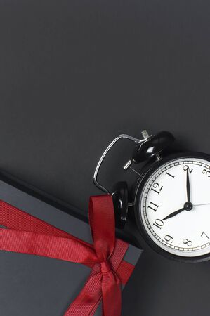 Black retro alarm clock and gift box with red ribbon on gray dark backgroundの写真素材