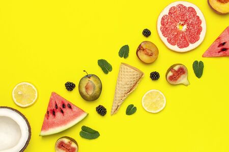 Tropical Summer Fruit Concept. Creative layout made of fresh ripe watermelon, peach, plum, fig, lemon, grapefruit, waffle ice cream cup, mint leaves on yellow background. Flat lay top view copy space.の写真素材