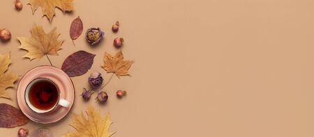 Autumn Flat lay composition. Cup of tea, autumn dry bright leaves, roses flowers, orange circle, cones, decorative pomegranate, cinnamon sticks on brown beige backgroundの写真素材