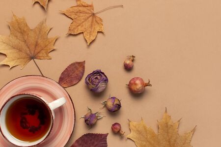 Autumn Flat lay composition. Cup of tea, autumn dry bright leaves, roses flowers, orange circle, cones, decorative pomegranate, cinnamon sticks on brown beige backgroundの写真素材