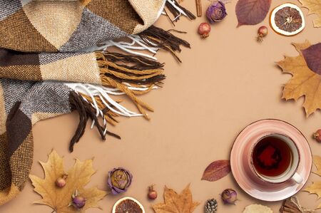 Autumn Flat lay composition. Cup of tea, checkered plaid, autumn dry leaves, roses flowers, orange circle cones decorative pomegranate cinnamon sticks on brown beige backgroundの写真素材
