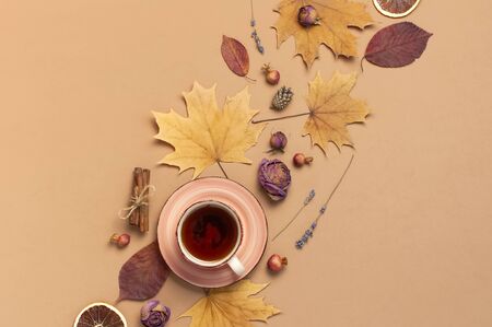 Autumn Flat lay composition. Cup of tea, autumn dry bright leaves, roses flowers, orange circle, cones, decorative pomegranate, cinnamon sticks on brown beige backgroundの写真素材