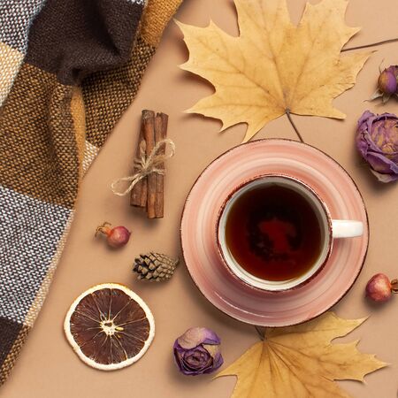 Autumn Flat lay composition. Cup of tea, checkered plaid, autumn dry leaves, roses flowers, orange circle cones decorative pomegranate cinnamon sticks on brown beige backgroundの写真素材