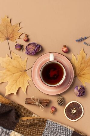 Autumn Flat lay composition. Cup of tea, checkered plaid, autumn dry leaves, roses flowers, orange circle cones decorative pomegranate cinnamon sticks on brown beige backgroundの写真素材