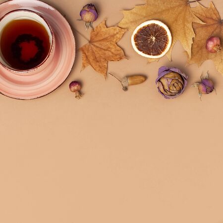 Autumn Flat lay composition. Cup of tea, autumn dry bright leaves, roses flowers, orange circle, cones, decorative pomegranate, cinnamon sticks on brown beige backgroundの写真素材