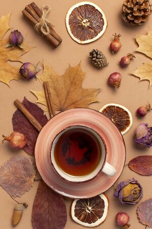 Autumn Flat lay composition. Cup of tea, autumn dry bright leaves, roses flowers, orange circle, cones, decorative pomegranate, cinnamon sticks on brown beige backgroundの写真素材