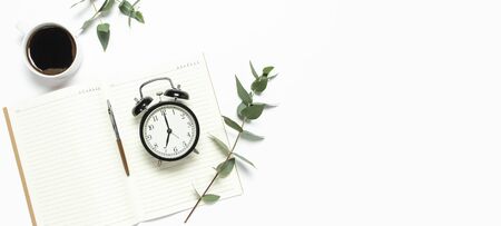 Flat lay cup of black coffee, black alarm clock, notebook, diary, eucalyptus on white backgroundの写真素材
