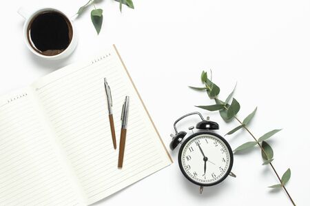 Flat lay cup of black coffee, black alarm clock, notebook, diary, eucalyptus on white backgroundの写真素材