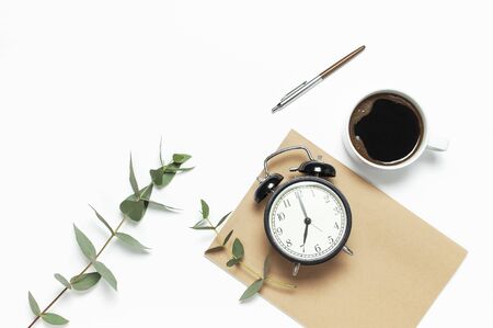 Flat lay cup of black coffee, black alarm clock, notebook, diary, eucalyptus on white background top view copy space.の写真素材