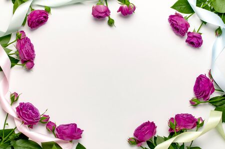 Flat lay flowers composition. Frame made of bright pink rose flowers and colorful holiday ribbons on light gray background top view copy space.の写真素材