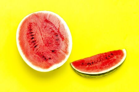 Half and pieces of ripe juicy red watermelon on bright yellow background. Flat lay, top view, copy space.の写真素材