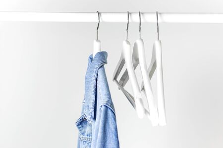 Blue denim jacket on white wooden coat hanger on a rod against light gray wall flat lay copy space. Denim, fashionable jacket, women's or men's trend clothing, fashion background. Store concept, sale.の写真素材