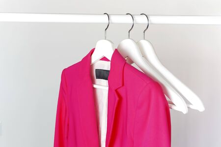 Bright pink women's jacket on white wooden coat hanger on rod against light gray wall flat lay copy space. Fashionable jacket, women's trend clothing, fashion background. Store concept, sale.の写真素材