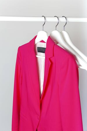 Bright pink women's jacket on white wooden coat hanger on rod against light gray wall flat lay copy space. Fashionable jacket, women's trend clothing, fashion background. Store concept, sale.の写真素材