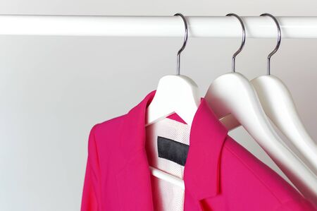 Bright pink women's jacket on white wooden coat hanger on rod against light gray wall flat lay copy space. Fashionable jacket, women's trend clothing, fashion background. Store concept, sale.の写真素材