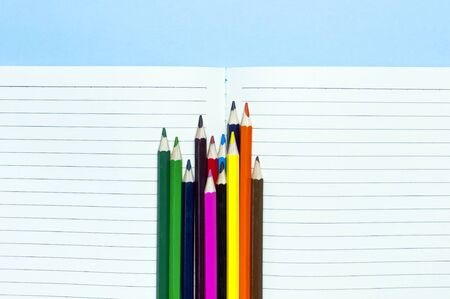 Back to school concept. Color pencils and clean notebook in line on blue background top view flat lay copy space. Wooden colored pencils for drawing, objects for creativity, school supplies close-up.の写真素材