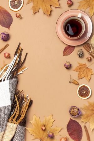 Autumn Flat lay composition. Cup of tea, checkered plaid, autumn dry leaves, roses flowers, orange circle cones decorative pomegranate cinnamon sticks on brown beige background top view. Fall concept.の写真素材