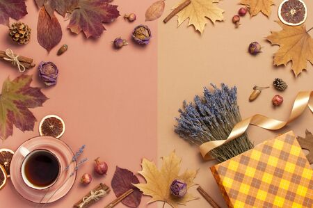 Autumn Flat lay composition. Cup of tea, autumn dry leaves, roses flowers, lavender, gift bag cones decorative pomegranate cinnamon sticks on brown pink background top view. Autumn, fall concept.の写真素材