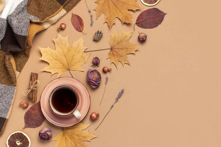Autumn Flat lay composition. Cup of tea, checkered plaid, autumn dry leaves, roses flowers, orange circle cones decorative pomegranate cinnamon sticks on brown beige background top view. Fall concept.の写真素材
