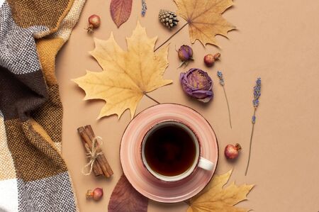 Autumn Flat lay composition. Cup of tea, checkered plaid, autumn dry leaves, roses flowers, orange circle cones decorative pomegranate cinnamon sticks on brown beige background top view. Fall concept.の写真素材