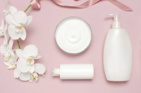 Beauty Spa concept. Opened container with cream, cosmetic bottle containers, white Phalaenopsis orchid flowers on pink background Flat lay top view. Herbal dermatology cosmetic hygienic cream.の写真素材