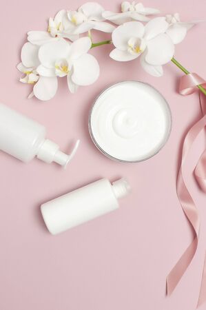 Beauty Spa concept. Opened container with cream, cosmetic bottle containers, white Phalaenopsis orchid flowers on pink background Flat lay top view. Herbal dermatology cosmetic hygienic cream.の写真素材