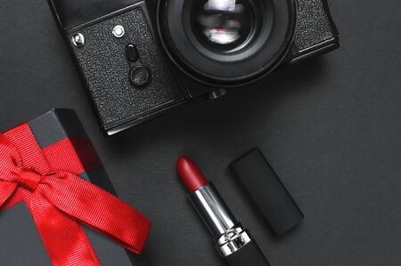 Old retro vintage camera, Black gift box with red ribbon, red lipstick on black background top view flat lay with copy space. Concept for the photographer, old photographic equipment, present.の写真素材