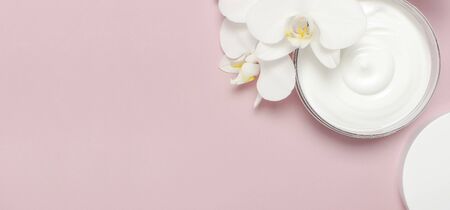 Beauty Spa concept. Opened plastic container with cream and White Phalaenopsis orchid flowers on pink background Flat lay top view. Herbal dermatology cosmetic hygienic cream, organic cosmetic Natural.の写真素材