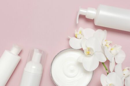 Beauty Spa concept. Opened container with cream, cosmetic bottle containers, white Phalaenopsis orchid flowers on pink background Flat lay top view. Herbal dermatology cosmetic hygienic cream.の写真素材