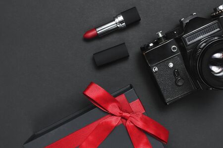 Old retro vintage camera, Black gift box with red ribbon, red lipstick on black background top view flat lay with copy space. Concept for the photographer, old photographic equipment, present.の写真素材