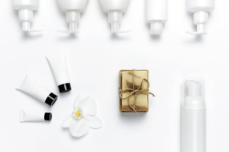 White cosmetic bottle containers, natural soap, orchid flower on white background top view flat lay. Cosmetics SPA branding mock-up. Natural organic beauty product concept. Minimalism cosmetics style.の写真素材