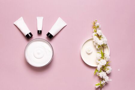 Beauty Spa concept. Opened plastic container with cream, cosmetic bottle containers, spring White flowers on pink background Flat lay top view. Herbal dermatology cosmetic hygienic cream organic.の写真素材