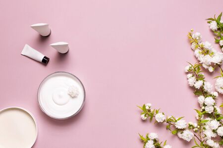 Beauty Spa concept. Opened plastic container with cream, cosmetic bottle containers, spring White flowers on pink background Flat lay top view. Herbal dermatology cosmetic hygienic cream organic.の写真素材