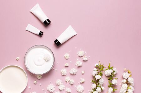 Beauty Spa concept. Opened plastic container with cream, cosmetic bottle containers, spring White flowers on pink background Flat lay top view. Herbal dermatology cosmetic hygienic cream organic.の写真素材