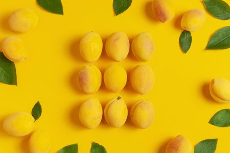 Frame from ripe fresh apricots fruits with green leaves on yellow background. Flat lay, top view, copy space. Fresh organic apricots, diet vegan food. Creative Apricot pattern. Harvest concept.の写真素材