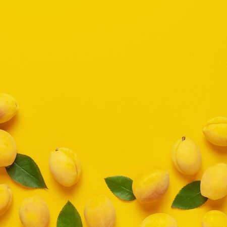 Ripe fresh apricots fruits with green leaves on yellow background. Flat lay, top view, copy space. Fresh organic apricots, diet vegan food. Creative Apricot pattern. Harvest concept.の写真素材