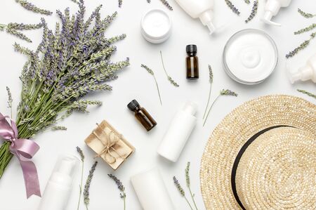 Concept of natural spa cosmetics. Open jar of cream, white cosmetics bottles, soap, straw hat and bouquet of lavender on white background top view copy space. Natural herbal skin care products.の写真素材