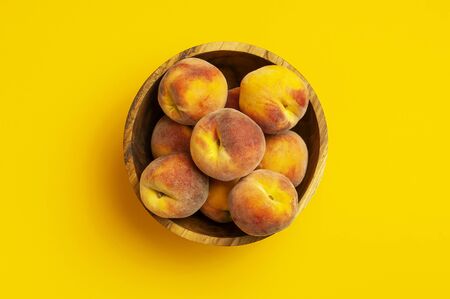 Flat lay composition with peaches. Ripe juicy peaches in wooden bowl on yellow background. Flat lay, top view, copy space. Fresh organic fruit, vegan food. Harvest concept.の写真素材